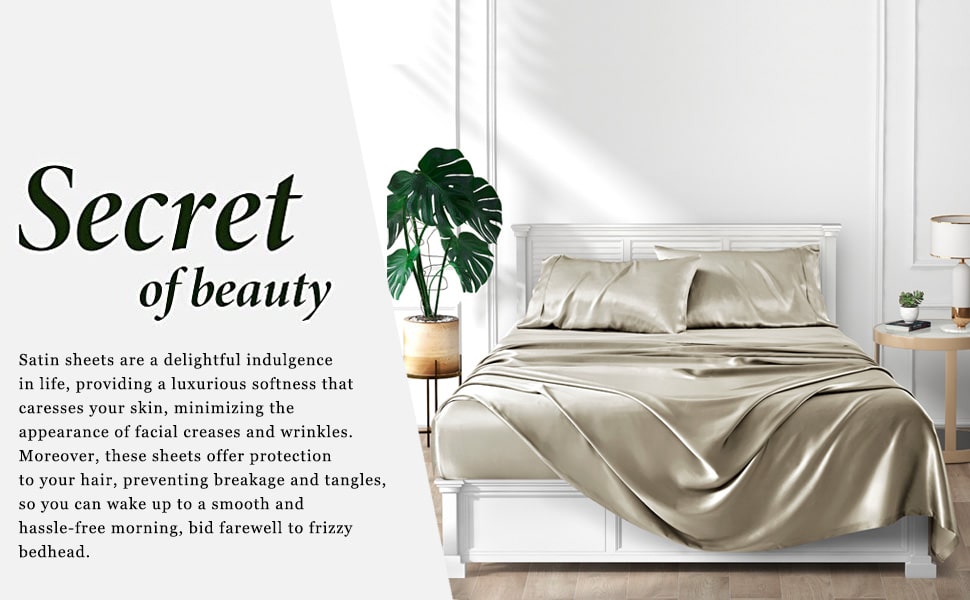 Taupe satin sheets on white bed next to green plant and night stand with white light on it.