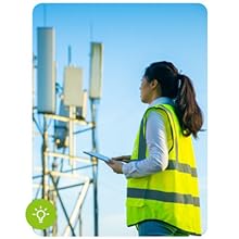 Female engineer in neon vest looking at cell tower